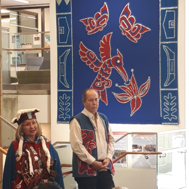 Elders stand in front of button blanket in Library