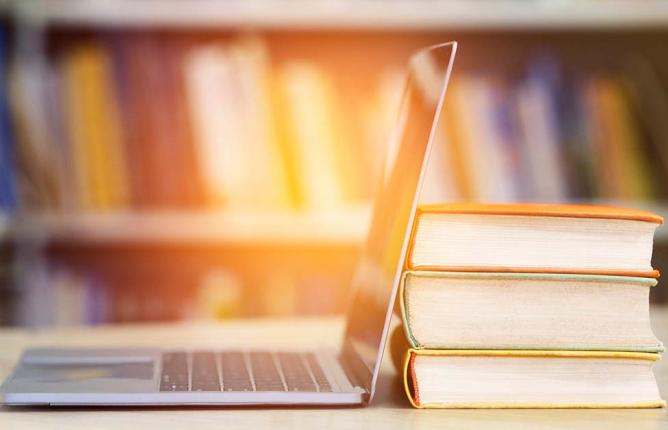 Laptop leaning up against books, book shelves in backgorun