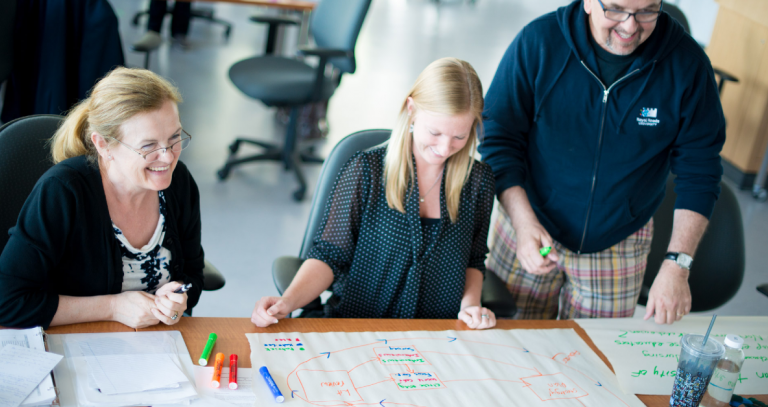 Three people working on flip chart paper with coloured markers