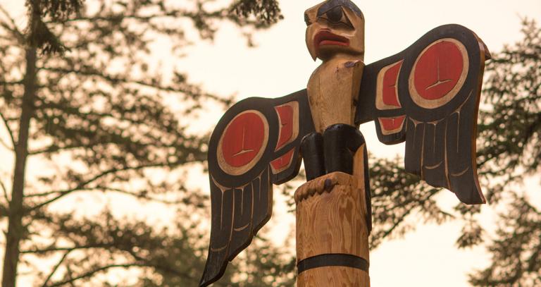 Totem poll with trees in background at sunset