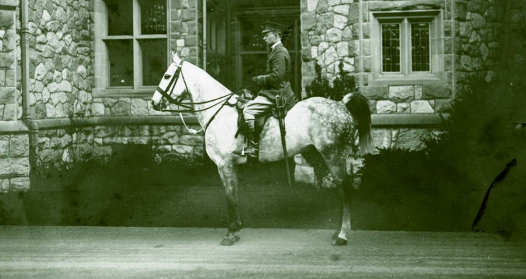 Archival photo of person on horseback in front of stone building