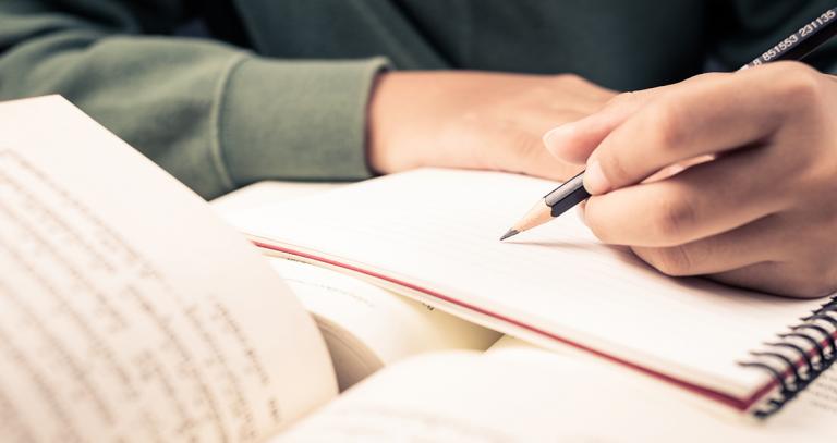 Person writing in notebook while consulting article