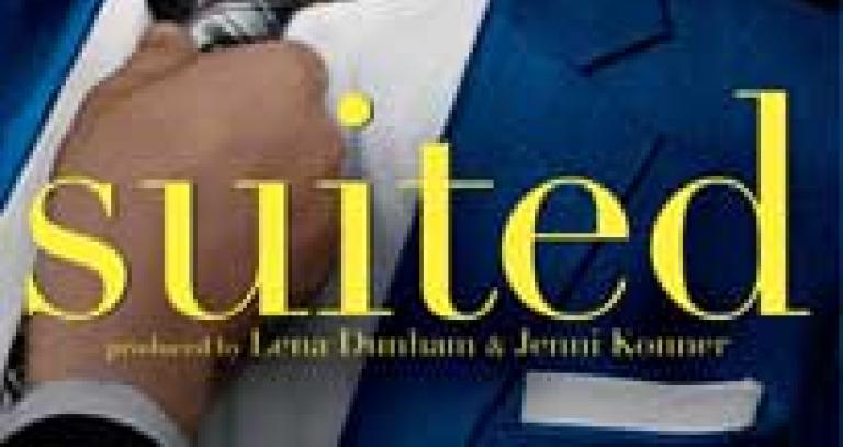 Close-up of a person's torso wearing a suit-jacket and tie. Someone else's hand is adjusting the tie. The word "Suited" appears in front.